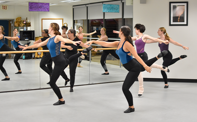 Students practice in a jazz class, wearing blue leotards and black tights